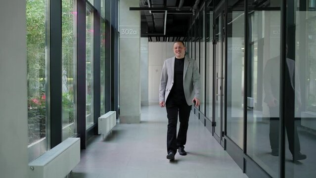 Happy businessman walking in office corridor. Man walks down office corridor, radiating confidence and professionalism. Business concept.