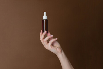 Hand holding serum glass bottle or essential oil on brown background. Natural Organic Spa Cosmetic concept