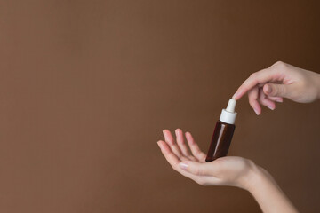 Hand holding serum glass bottle or essential oil on brown background. Natural Organic Spa Cosmetic concept