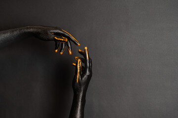 Woman's hands with black and gold paint on her skin on dark background. High Fashion art concept