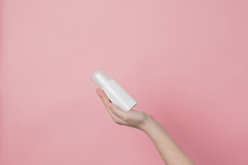 White unbranded cream bottle with pump in hand on pink background. Concept of beauty. Product cosmetic advertising