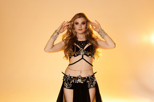 A captivating young woman in a stunning black and gold costume gracefully performs a mesmerizing belly dance.