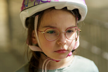 Little cute sad girl cyclist wearing glasses and a helmet