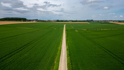 An aerial view of a road cutting through green fields under a cloudy sky, showing a serene rural landscape