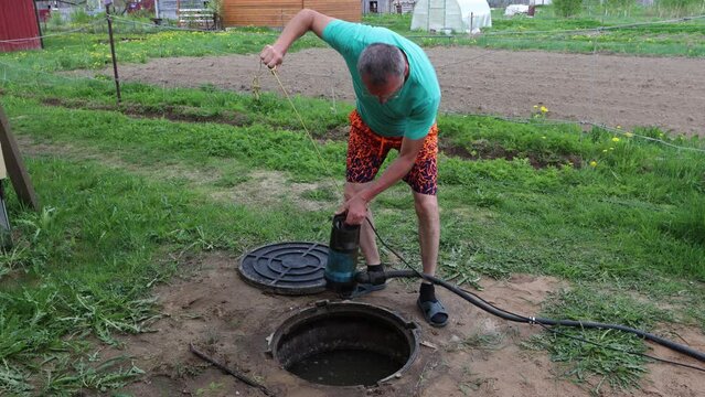 Homeowner pumping sewage waste from septic tank with wastewater pump through maintenance hole.