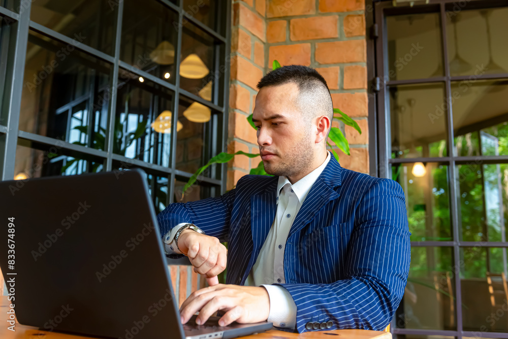 Wall mural male businessman working on laptop conferencing with the customer checking the time on his watch. th