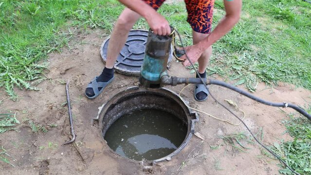 Man lowers wastewater pump into septic tank to pumping sewage.