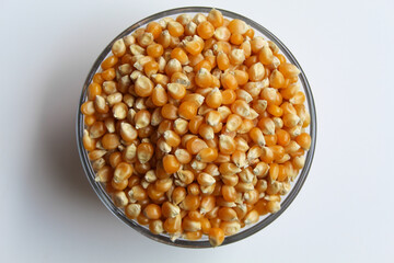 Dried corn kernels full in glass transparent bowl, isolated on white background, flat lay or top view