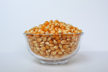 Dried corn kernels full in glass transparent bowl, isolated on white background