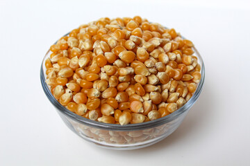 Dried corn kernels full in glass transparent bowl, isolated on white background