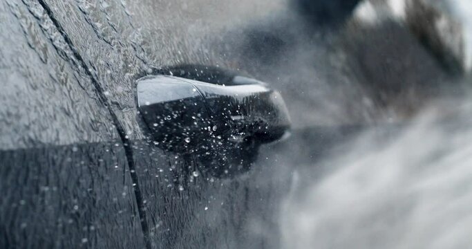 Super slow motion macro of modern auto vehicle detail under high pressure water jet during washing process on self service car wash. Manual car wash with pressurized water spray.