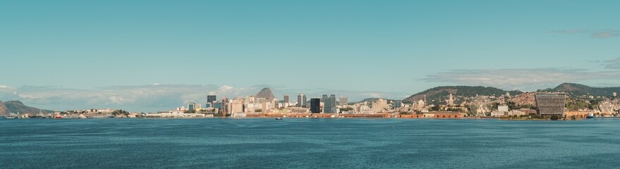 Fototapeta premium Panoramic view of Rio de Janeiro, Brazil, showcasing the city's skyline against a clear blue sky. The image features iconic buildings, lush hills, and the vast expanse of Guanabara Bay