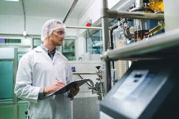 A man in a white lab coat is writing on a clipboard in front of a machine. Concept of focus and concentration as the man takes notes while working in a laboratory setting