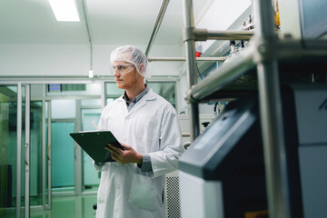 A man in a lab coat holding a clipboard. He is wearing a white lab coat and a white hat