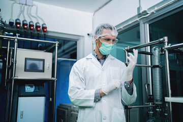 A man in a white lab coat is wearing a mask and gloves. He is holding a test tube in his right hand