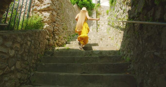 Woman ascends stone steps in a quaint Ravello town in Italy. Girl moves forward and invites you to follow her to explore narrow historical pathways.