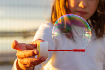 Hand of a white girl holding a soap bubble in the air. Traditional and universal children's games.