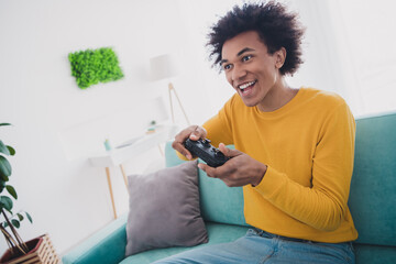 Photo of excited cool cheerful man sitting divan playing game spending weekend home rest relax...