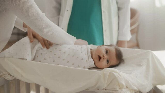 A young mother swaddles a baby with a white blanket on a table in the hospital