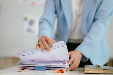 Portrait of a young Asian business woman working on Stacks of paper files to find and check...