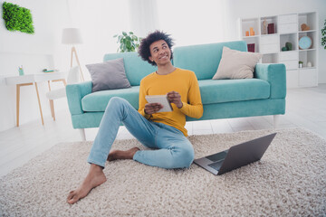 Full size photo of nice young man sit floor hold notepad laptop wear yellow pullover white interior...