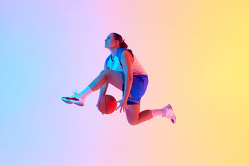 Dynamic photo of young basketball player leaping to make powerful slam dunk in neon light against gradient studio background. Concept of professional sport, championship, hobby and recreation. Ad