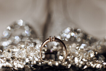 A gold ring sits on a pile of glittering jewels. The ring is the center of attention, and the...