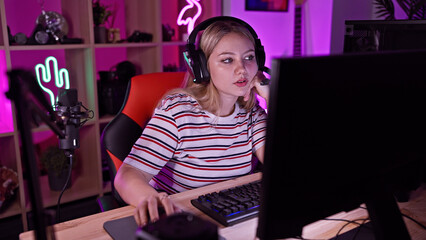 Focused young woman with headphones using computer in a neon-lit gaming room at night.