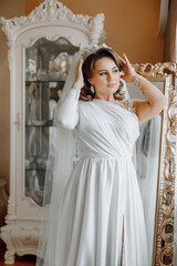 A woman in a white dress is getting ready for a wedding. She is putting on a tiara and adjusting...