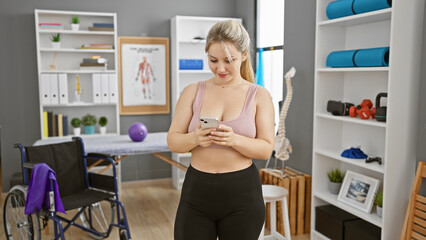 A young woman uses her smartphone in a rehab clinic's therapy room, conveying a sense of modern healthcare.