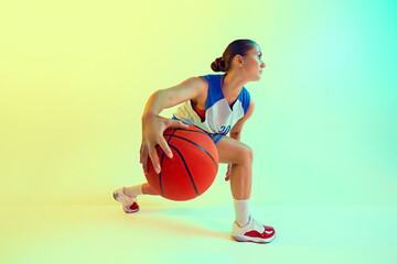 Photo of woman in blue and white basketball jersey, focused and dribbling ball in neon light against gradient studio background. Concept of sport, championship, tournament, hobby and recreation. Ad © Lustre Art Group 