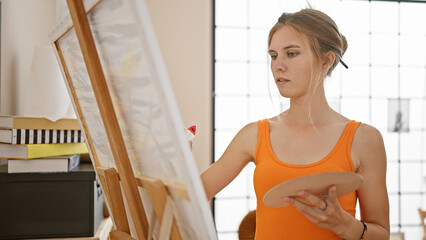 A focused young woman artist painting in a bright studio with large windows.