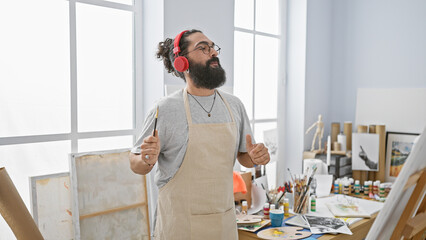 Hispanic man with beard and headphones enjoys painting in a bright art studio.