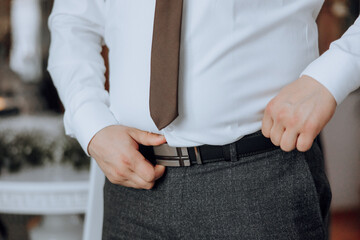 A man in a white shirt and a brown tie is adjusting his pants. Concept of formality and attention...