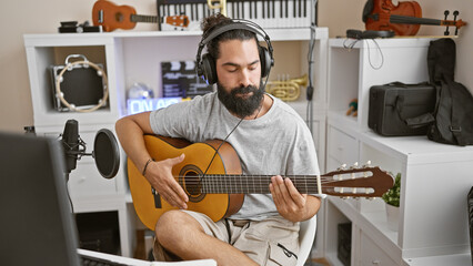 Hispanic man playing guitar in a home music studio with microphone and headphones © Krakenimages.com
