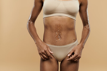 Pretty, slim African American woman standing in bra and panties on beige background.