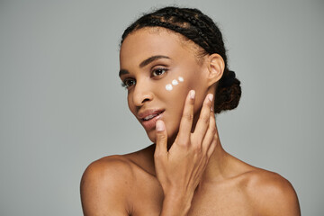 Young African American woman with cream-covered face, focused on skincare routine, in a strapless...