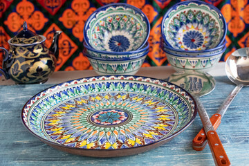 Beautiful hand painted ceramic dish with ornament in Central Asian style. slotted spoon and ladle on blue table.