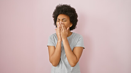 A young black woman covers her mouth with her hands against a pink background, conveying emotion or...