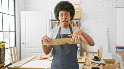 African american woman examining a wooden plank in a bright carpentry workshop