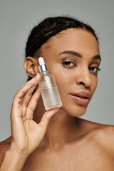 Beautiful young African American woman in strapless top holding serum to her face with focused care.