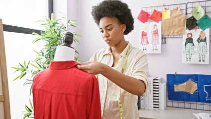 African woman tailor measuring garment on mannequin in bright atelier