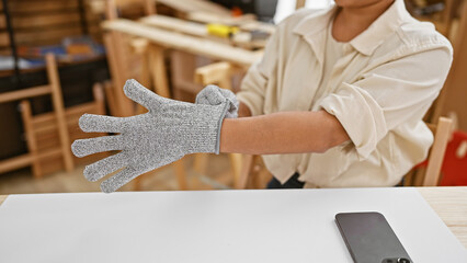 Fototapeta premium Captivating portrait, young, beautiful hispanic woman, a professional carpenter, wearing safety gloves, masterfully molding timber into furniture, sitting at carpentry table in her artistic workshop.