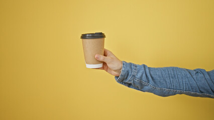 A hand in a denim sleeve extends a cardboard coffee cup against a yellow background, denoting informality and a casual setting.