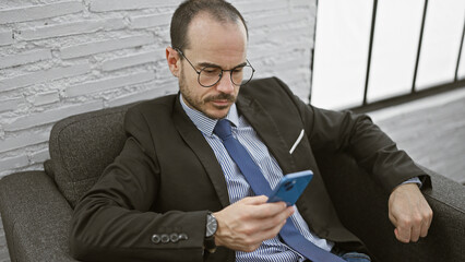 Bald businessman in suit using smartphone in office lounge