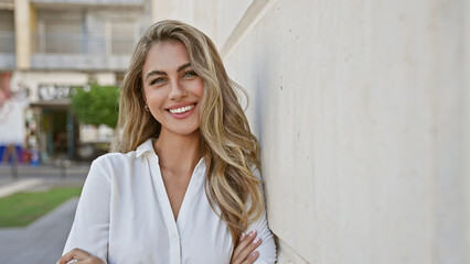 Laughing out loud, vivacious young blonde woman, confidently standing with her arms crossed in an...