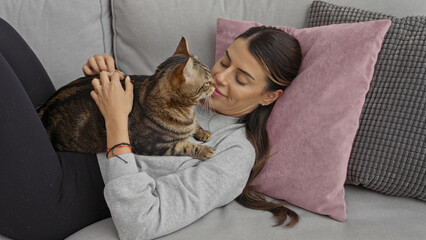 A young hispanic woman enjoys a relaxing moment with her kitten on a comfortable couch in the...