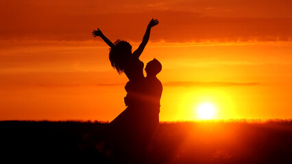 Silhouette of a couple in love against the background of a sunset in a field. Romantic scene of lovers. The concept of a love story, spending time together and feelings.