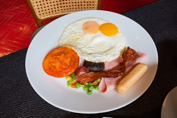 A Delicious and Hearty Breakfast Plate with Fried Eggs, Bacon, Sausage, Ham, Tomato, and Vegetables