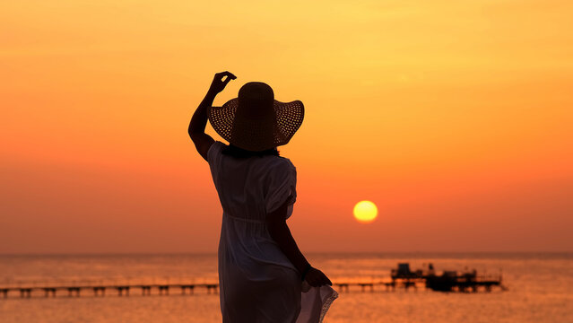 A strong, confident, beautiful woman under the rays of the setting sun on the ocean. Travel, femininity and relaxation concept.